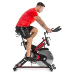 Mies polkee Gymstick FTR-7 spinningpyörällä punaisessa T-paidassa